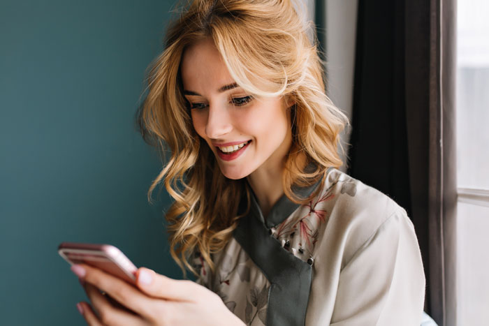 Smiling woman reading stories about women doing crazy things to get a crush to like them on her phone.