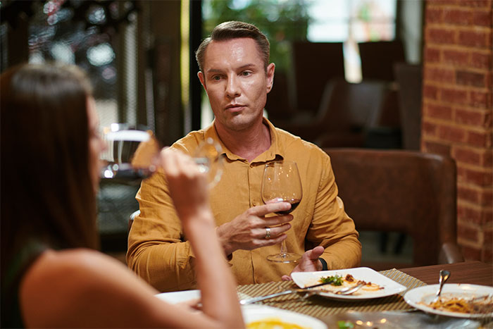 A man in a restaurant on a first date, looking awkward while holding a glass of red wine.