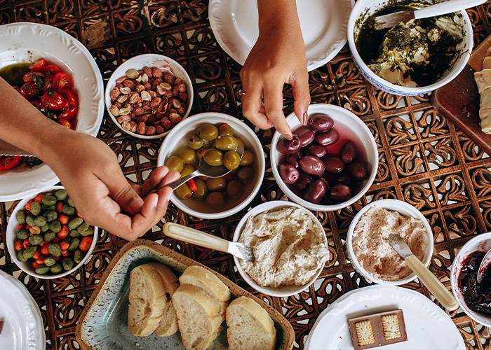 A spread of Mediterranean diet foods with hands serving olives and other dishes.