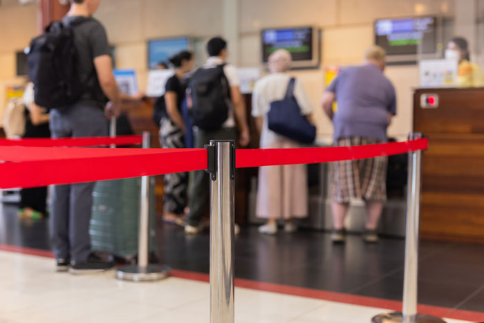 People stand in line at a service counter, a red velvet rope in the foreground, showing karma's instant effect.