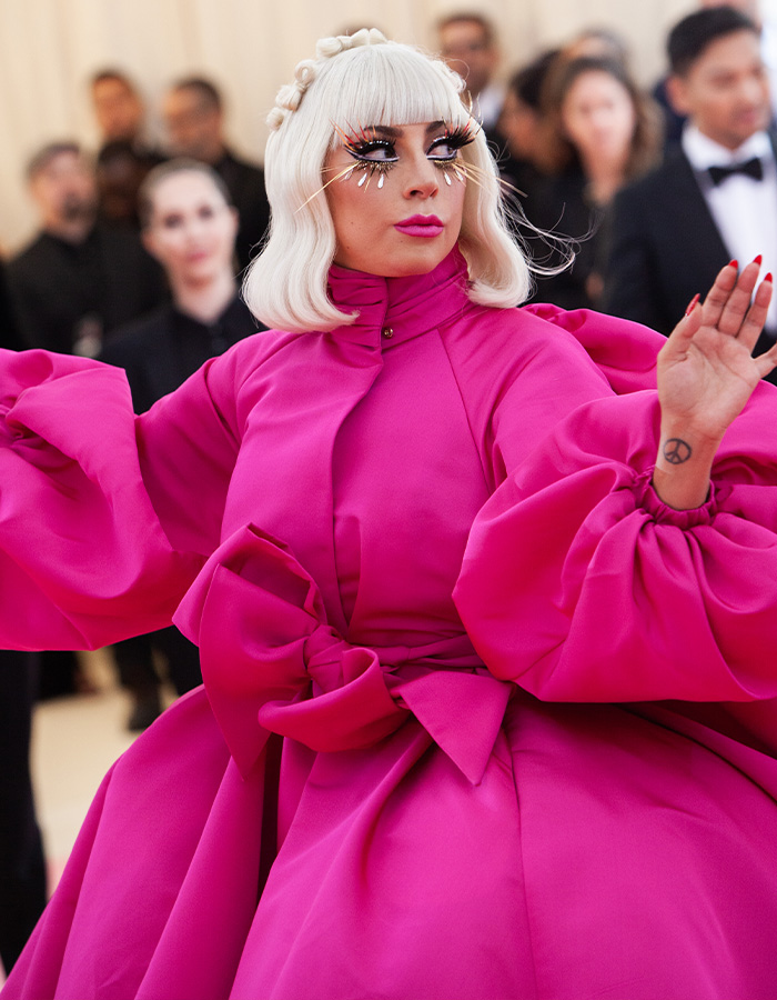 Lady Gaga expecting first baby. She wears a voluminous pink gown, with a crown and extravagant makeup.