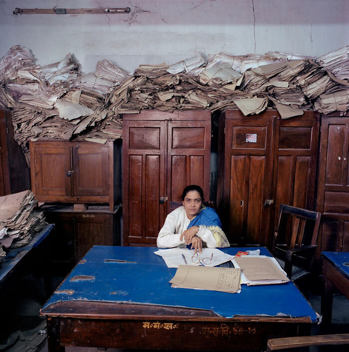 A photographer's project capturing a woman at a desk surrounded by large stacks of paperwork, reflecting global bureaucracy.