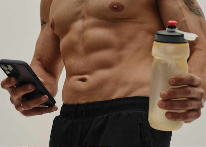 Fit man holding water bottle and phone, representing gym health issues affecting men's private parts