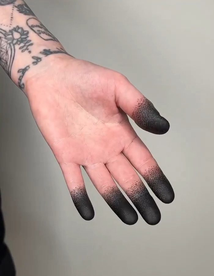 An open palm showing a viral fingertip tattoo trend with solid black ink on the tips. An open palm showing a viral fingertip tattoo trend with solid black ink on the tips.