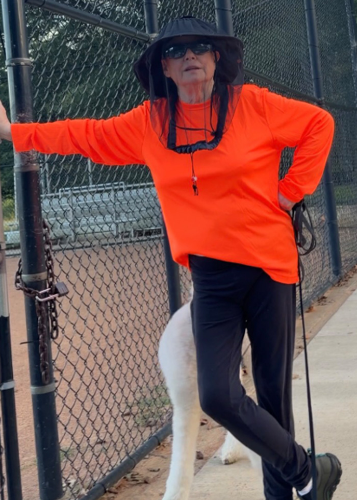 Woman in orange shirt and black hat leaning on locked field gate with dog Woman in orange shirt and black hat leaning on locked field gate with dog