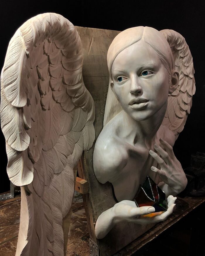 A lifelike sculpture of an angel holding a colorful pyramid by a Polish artist