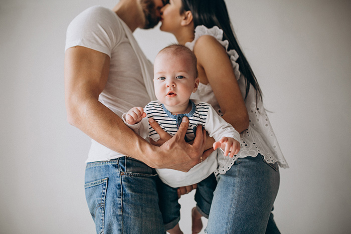Young family with baby boy and parents sharing a kiss, representing grandson and family relationships Young family with baby boy and parents sharing a kiss, representing grandson and family relationships