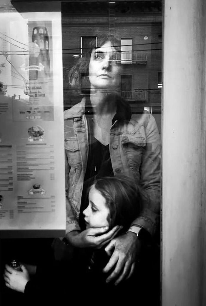 A mother and child reflected in a glass window, a visual story from Taylor Coble's street photos.