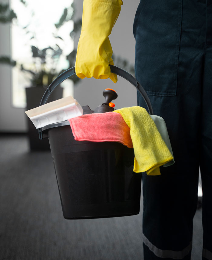 A worker in yellow gloves holding a cleaning bucket with colorful cloths, portraying moments workers are done.