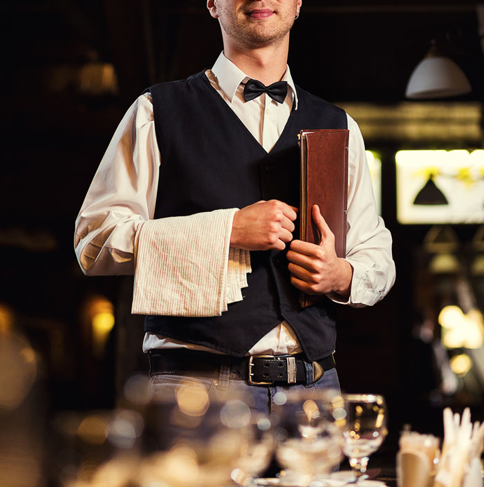 A waiter holding a menu and towel, representing service and stories about karma ensuring people get what they deserve.