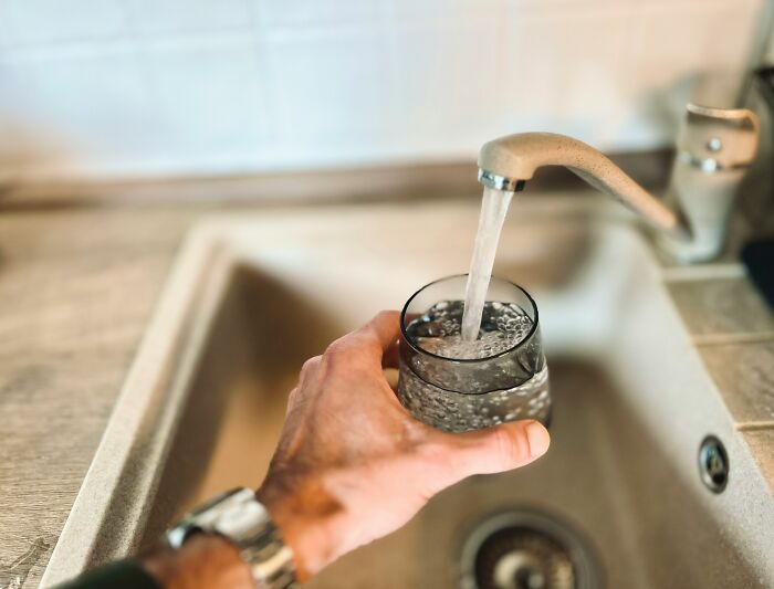 A hand holding a glass being filled with water from a kitchen faucet, relating to childhood beliefs about water.