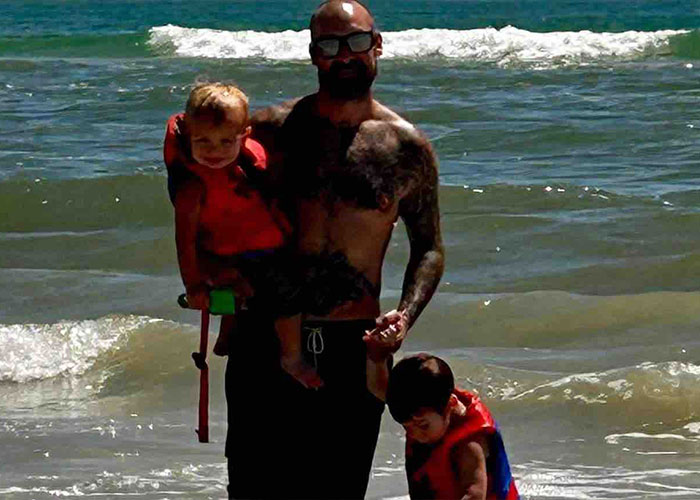 A father holds his young children in the ocean waves. The children's mother is identified as his attacker. A father holds his young children in the ocean waves. The children's mother is identified as his attacker.