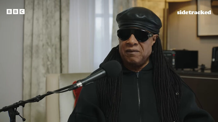 Stevie Wonder speaking at a microphone, illustrating stories of historical medical practices.