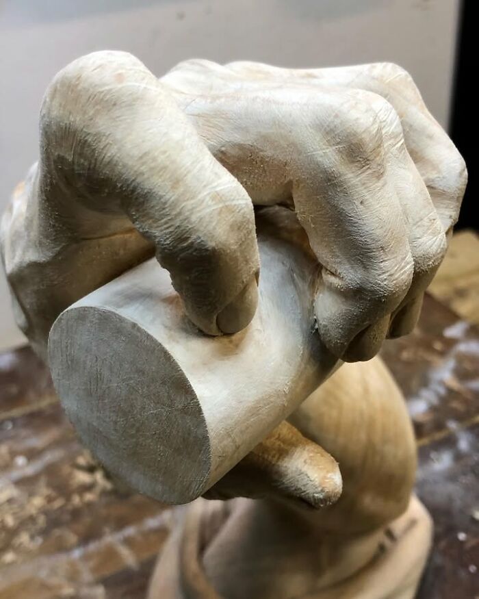 A Polish artist's detailed wood sculpture depicting a hand holding a cylinder