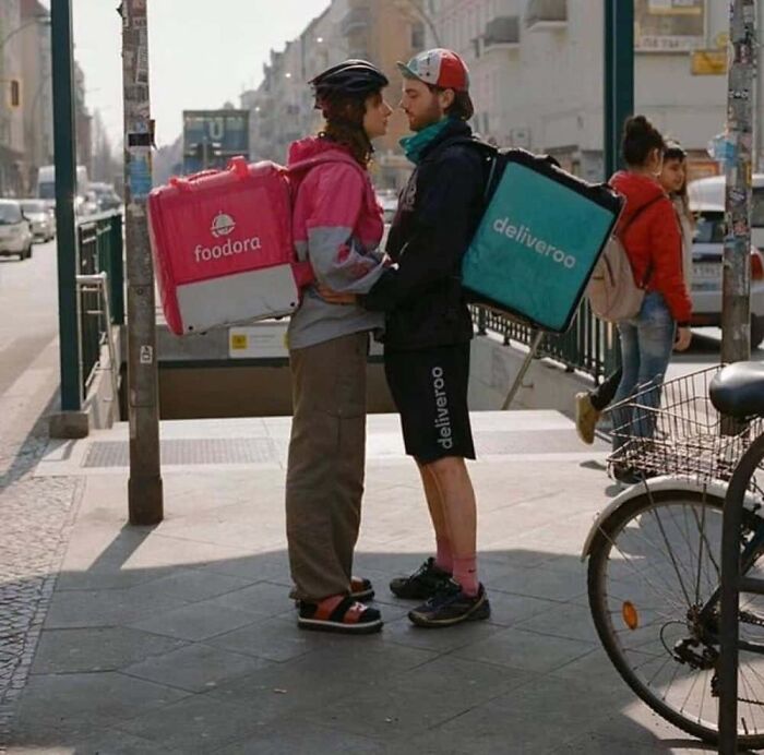 Hilarious photo of two food delivery drivers, one Foodora and one Deliveroo, sharing a kiss, embodying internet humor.