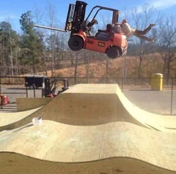 A forklift jumping over a ramp with a person hanging from it, a hilarious photo.