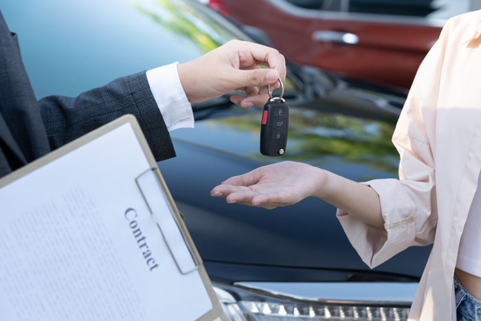 A handshake over a car key and a contract as a worker completes a deal, thinking 'I'm done'.