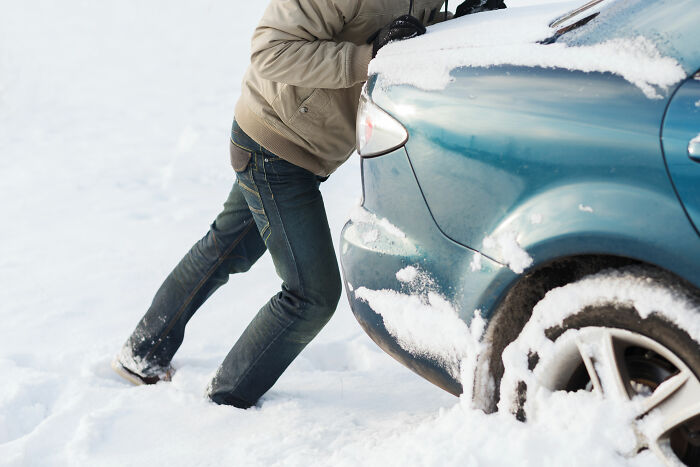 A person pushing a car stuck in deep snow, illustrating a moment of effort and tales of karma making people get what they deserve.