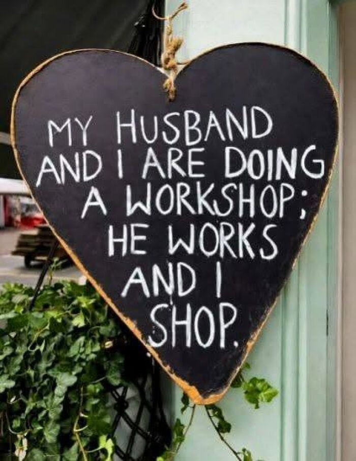A heart-shaped silly-funny-sign in chalk reads, My husband and I are doing a workshop: he works and I shop.