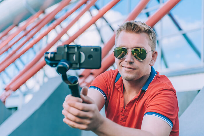 A man in sunglasses holding a phone on a gimbal, possibly demonstrating dumb ways people ruin their lives.