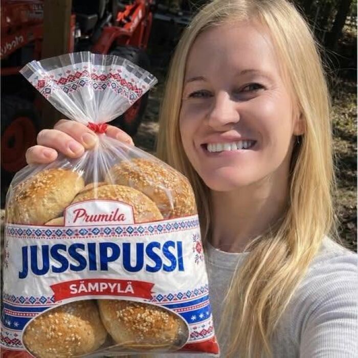 A woman smiling and holding a package of Prumila Jussipussi Sämpylä, a funny sign for bread.