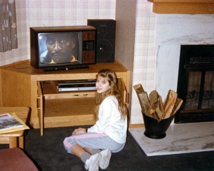 A girl sits on the floor in front of a retro tech TV and VCR, capturing an 80s moment.