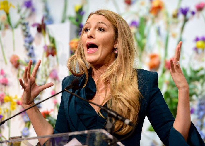 Blake Lively, a female star, at a podium, putting men in their place with blunt hand gestures.