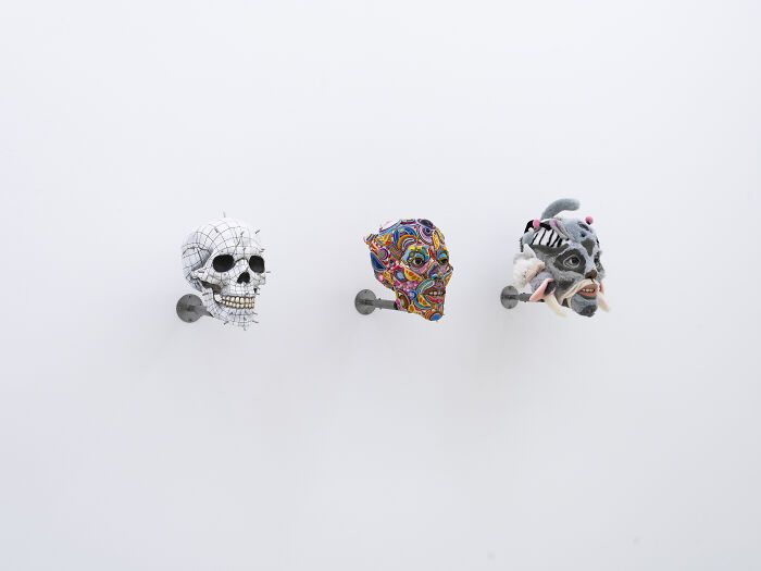 A gallery view of three unusual sculptures including a grid skull and vibrant thread-wrapped heads