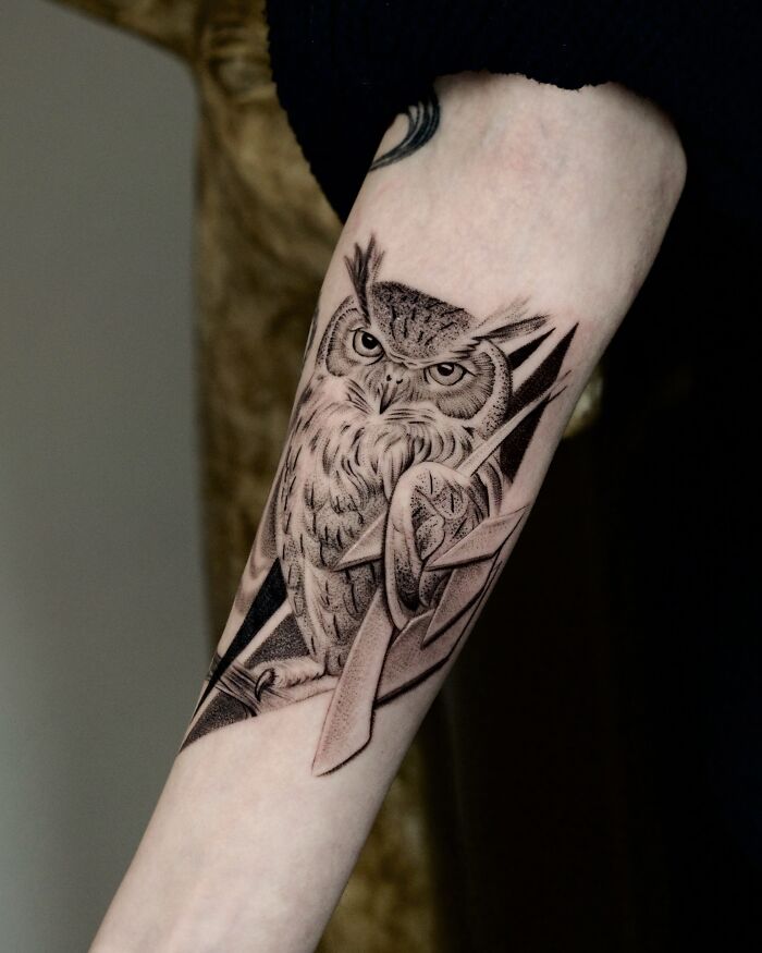 Intricate black ink owl tattoo with geometric shapes on arm