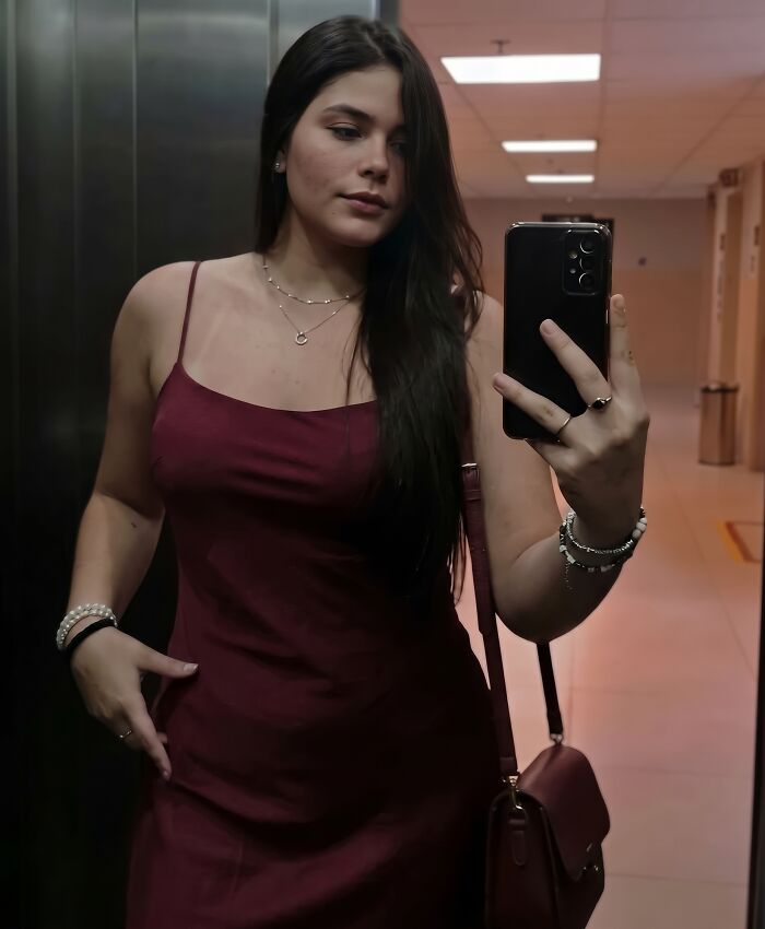 A 22YO daughter taking a selfie in a dark red dress inside an elevator. A 22YO daughter taking a selfie in a dark red dress inside an elevator.
