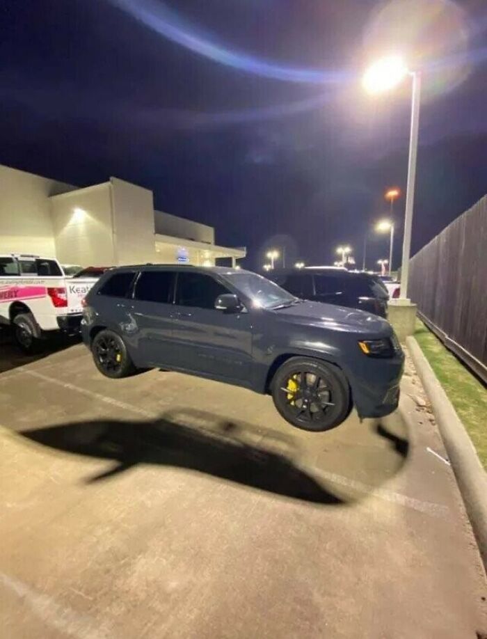 A gray SUV parked at night with a shadow that looks like a floating shark, making you look twice