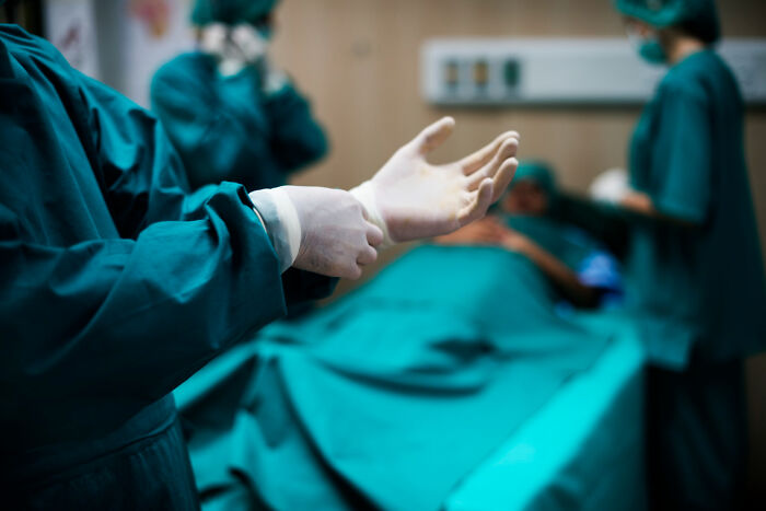 A surgeon putting on gloves, preparing for a standard medical procedure in an operating room.