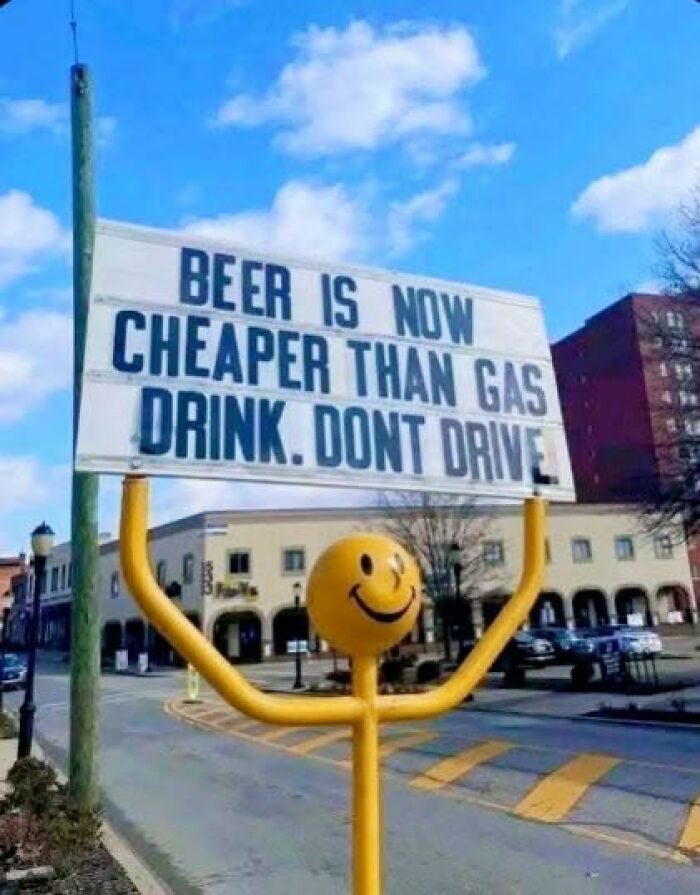 A funny sign with a smiley face statue, stating Beer is now cheaper than gas. Drink. Don't Drive.
