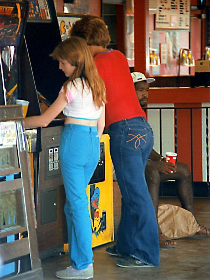 Two teenagers playing arcade games with 80s style fashion