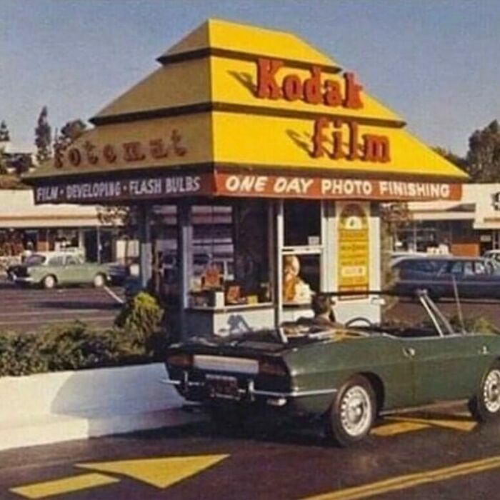 A vintage Kodak Film Fotomat drive-through kiosk with a green convertible car, representing '80s retro tech photography.