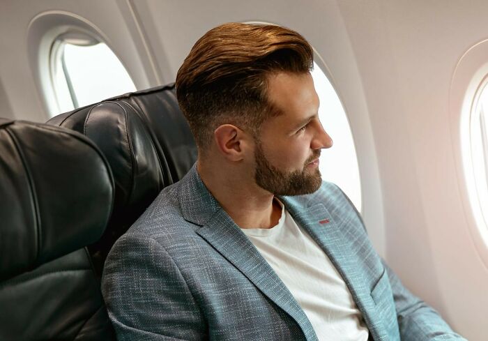 A male passenger looking out of a plane window during a flight