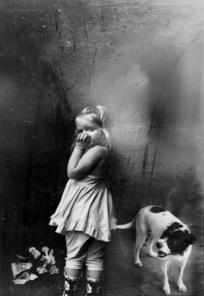 Black and white street photo by Taylor Coble showing a young girl with a shy expression next to a dog.