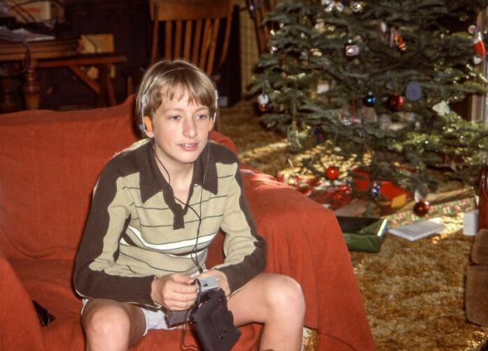 Boy playing handheld retro tech device by Christmas tree in 80s living room