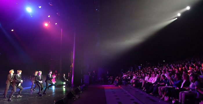 Men on stage, performing for a large audience, highlighting the complexities of relationships and headaches.