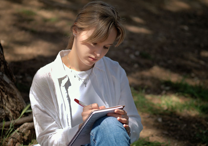 A young woman writing in a notebook, possibly detailing stories about women doing crazy things for a crush.
