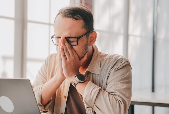 A tired worker thinking 'I'm done' covers their face, feeling exhausted at their laptop.