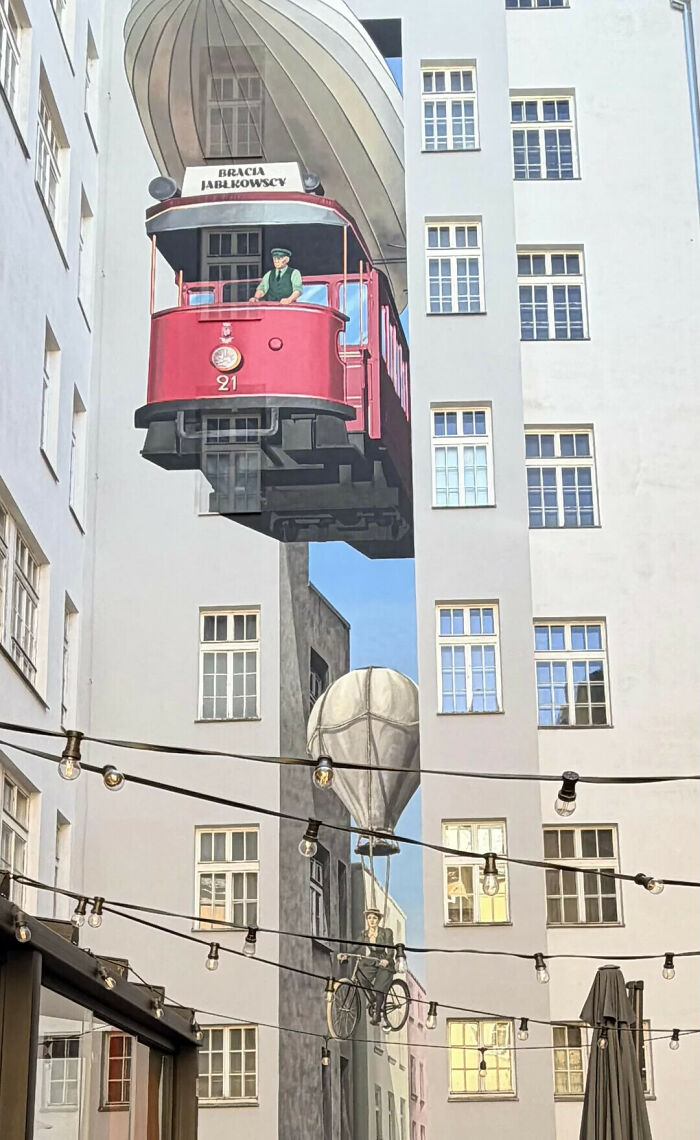 Mural of a red tram flying next to a building that might make you look twice to believe it.