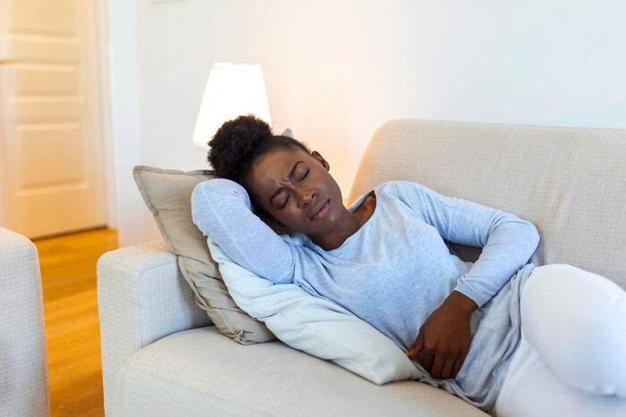 A woman on a sofa holding her stomach in pain, depicting the need for effective medical practices