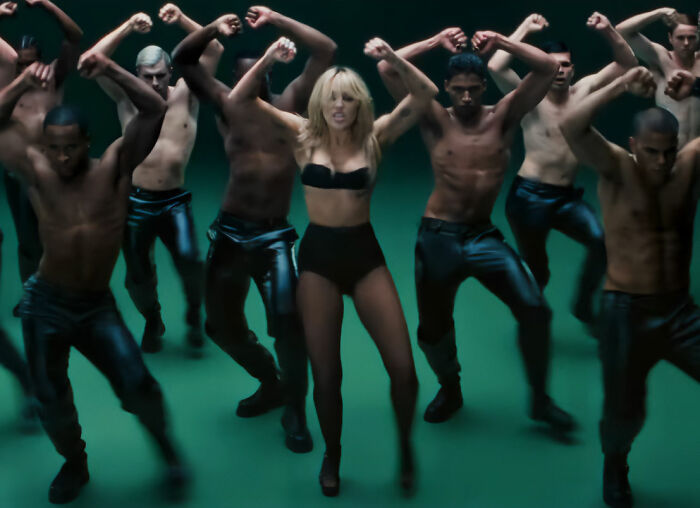 Miley Cyrus in black lingerie surrounded by shirtless male dancers, potentially reflecting the career after her name change. Miley Cyrus in black lingerie surrounded by shirtless male dancers, potentially reflecting the career after her name change.