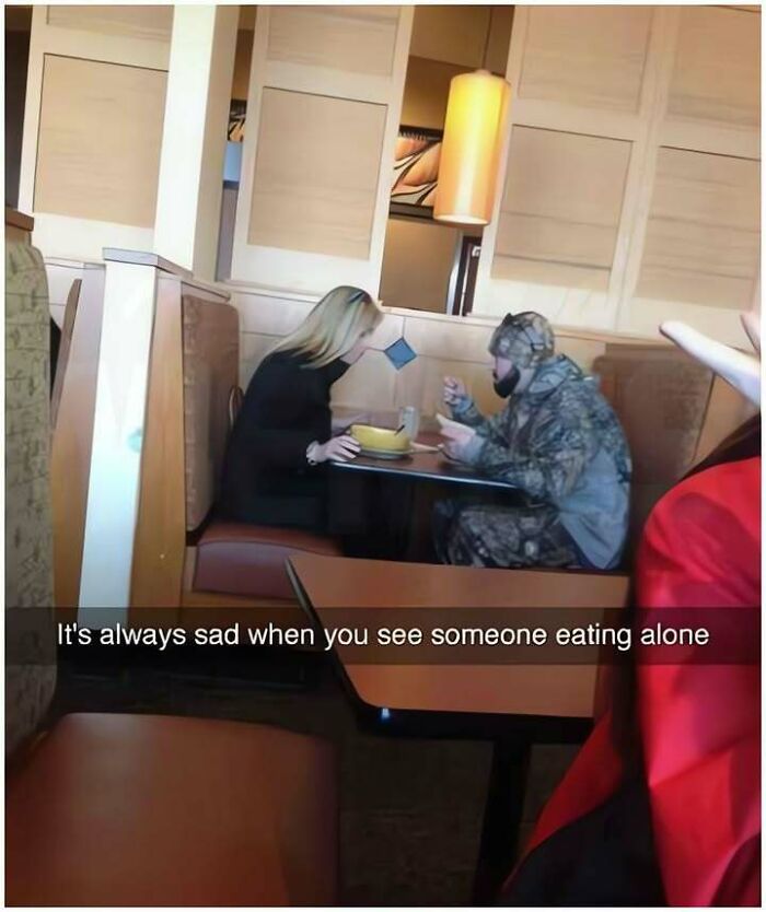 A woman leaning close to a man in camouflage at a restaurant, a funny meme about eating alone.