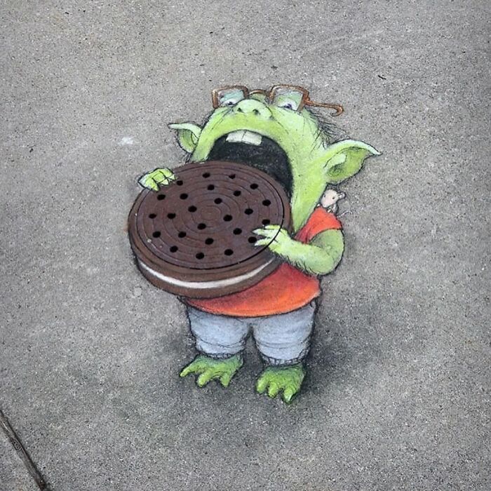 A captivating 3D street art drawing on the pavement, featuring a green goblin with glasses eating a giant cookie.