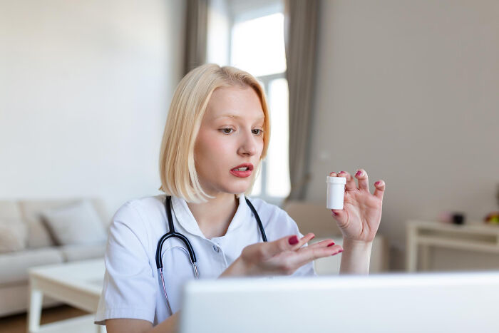 A female doctor on a video call, discussing problems society could face, holding a medicine bottle.
