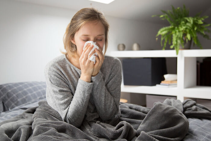 A young woman sneezing into a tissue, showing signs of a strange illness