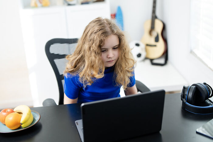 A young person with long hair intently looking at a laptop, considering problems society might face.
