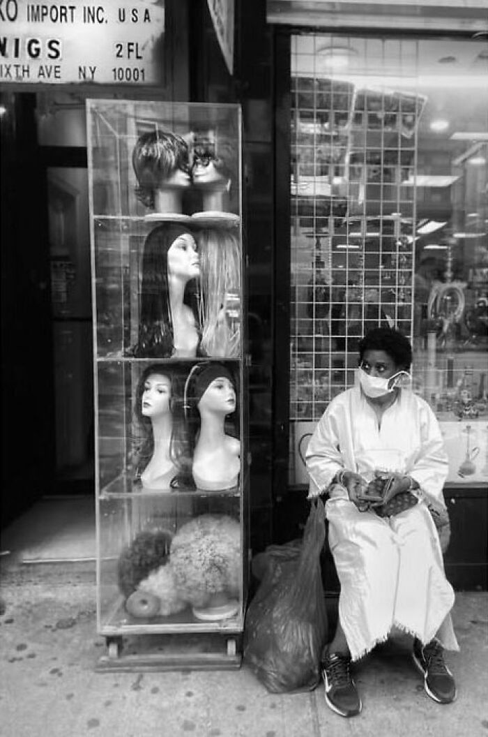 Street photo by Taylor Coble capturing a person in a mask sitting near a display of wigs, turning a fleeting moment into a visual story.